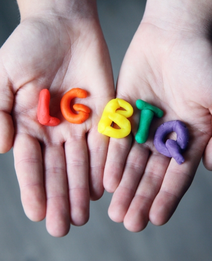 Hands holding colorful LGBTQ playdough letters